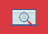 A magnifying glass with crosshairs over a laptop.